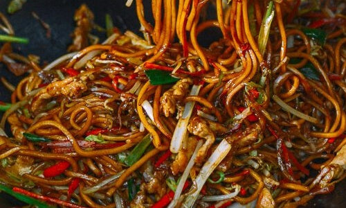 Lo mein met kip, witte kool, wortel en eiernoedels in een wok