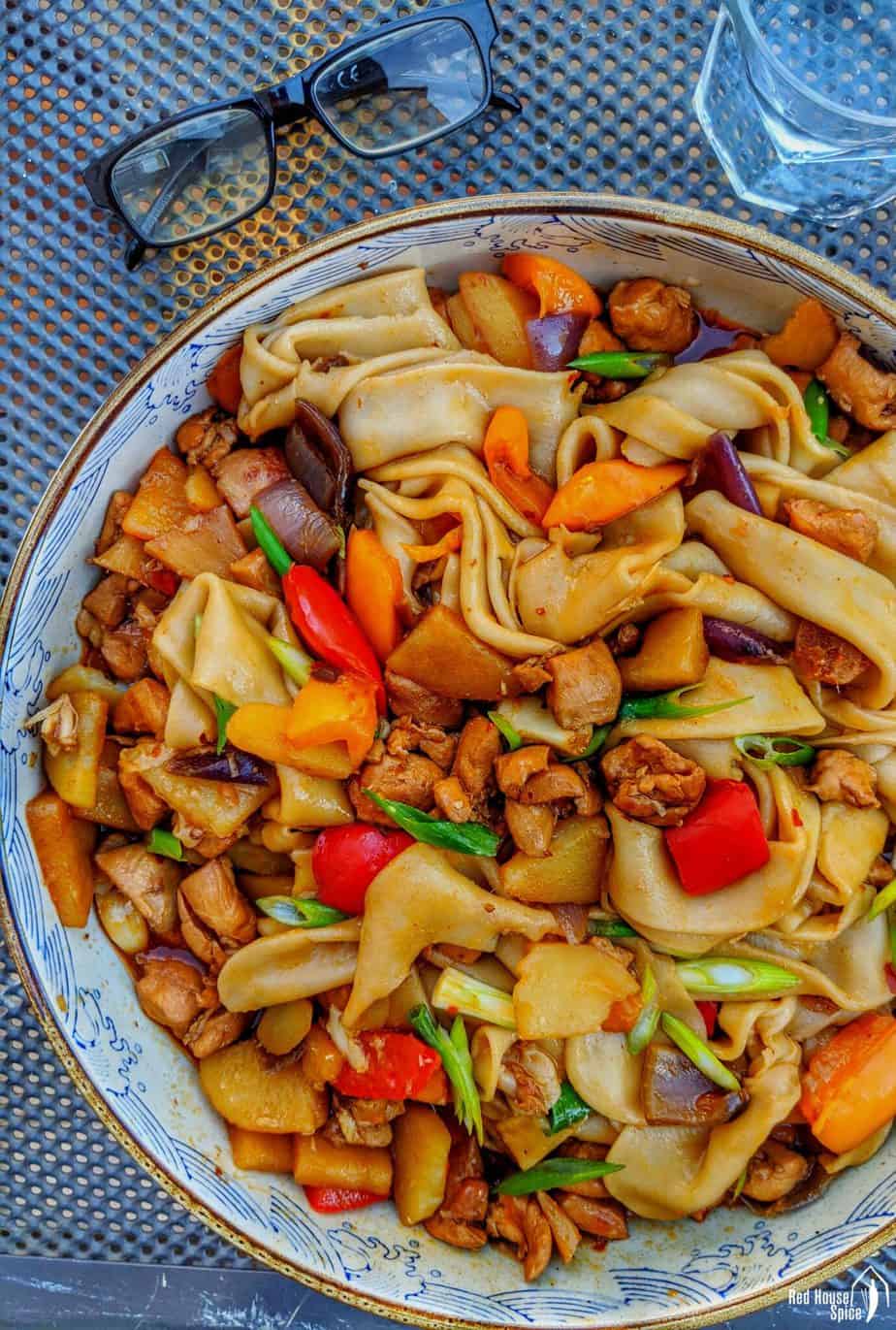 Kom noedels uit de wok met gestoofde Sichuan-kip, paprika en lente-ui