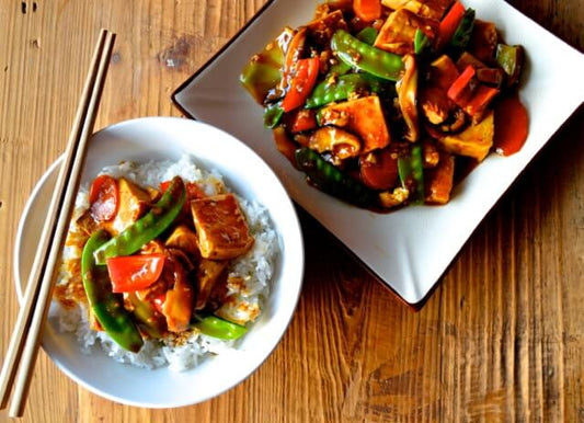 Gesmoorde tofu met suikererwten, wortel en paprika in een wok met glanzende saus